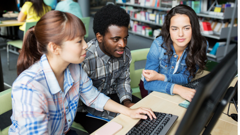 three high schoolers use a computer in the library
