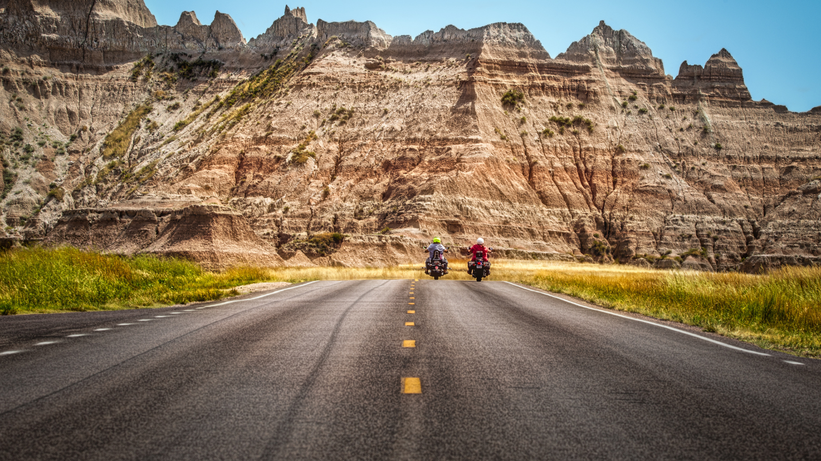 Two motorcycles on a road in front of mountains.